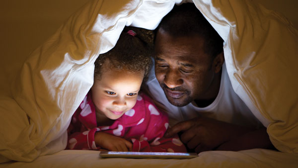 Father & Daughter Viewing Tablet Under Covers